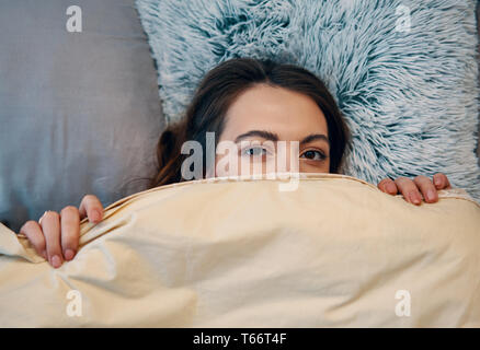 Portrait of young woman hide under blanket on a bed Stock Photo