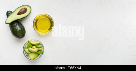 Whole and sliced avocado and oil in bowls on concrete background top view, copy space. Healthy recipes concept Stock Photo