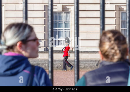 London, UK - October 3, 2018 - Back view of two tourists watching a sentry of Grenadier Guards patrolling outside Buckingham Palace Stock Photo