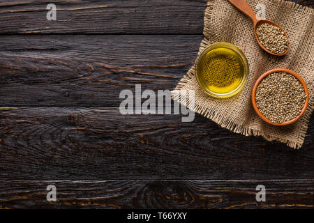 Hemp oil and hemp seeds in bowls on napkin over wooden background, top view, copy space. Naturopathy, medicine concept Stock Photo
