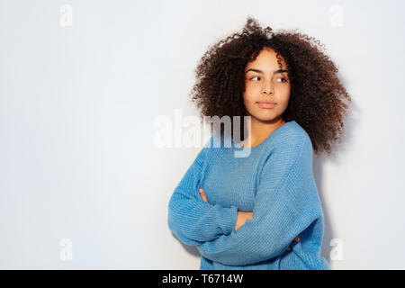 Portrait of thoughtful young black woman smiling standing against white wall Stock Photo