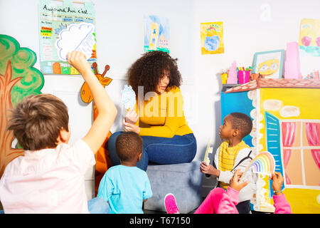 Group of kids with teacher hold and lift weather cards of rain snow rainbow as a game in kindergarten Stock Photo