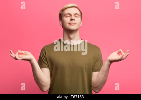 emotional attractive man feels relaxed, has rest, stands in meditative pose, mediates, enjoys calm and peaceful atmosphere. close up photo. isolated p Stock Photo
