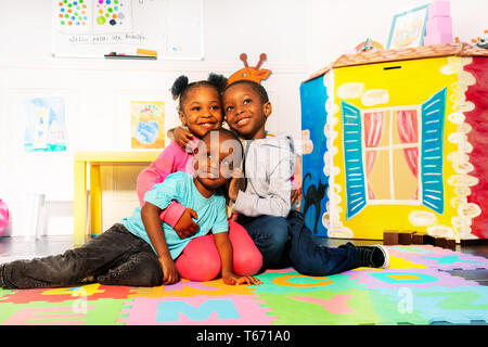 Group of three happy boys and girl in kindergarten hugging together Stock Photo