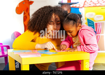 Teacher with little black boy in nursery school learning cursive alphabet by special tactile cards Stock Photo