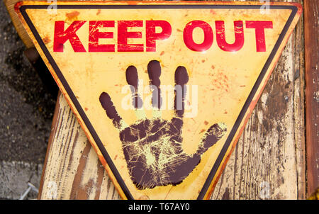 yellow triangular sign wih keep out in red and an open black hand in stop position, with a wooden background Stock Photo