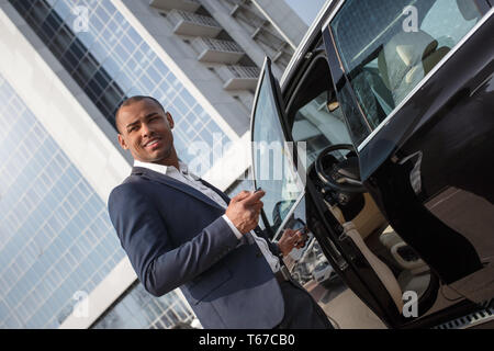 Young african american man standing near car opening door with alarm key looking aside smiling cheerful Stock Photo