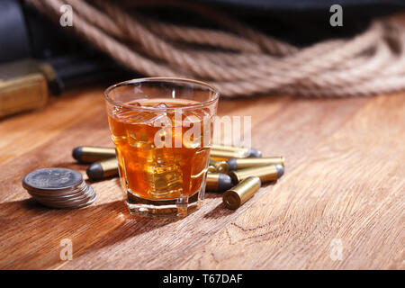 Wild west rifle and ammunitions with glass of whisky and ice with old silver dollar on wooden bar table Stock Photo