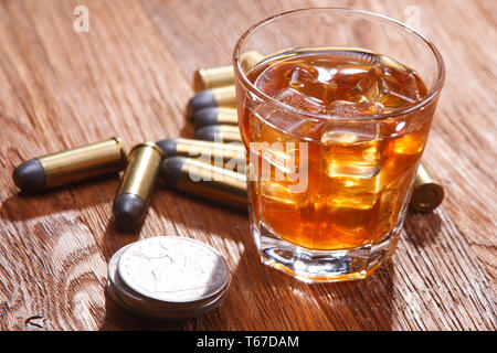 Glass of whisky and ice with ammunitions old silver dollar on wooden bar table Stock Photo