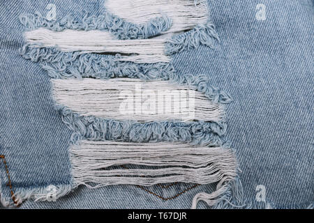 Hole and Threads on Denim Jeans. Ripped Destroyed Blue jeans background. Close up blue jean texture. Stock Photo
