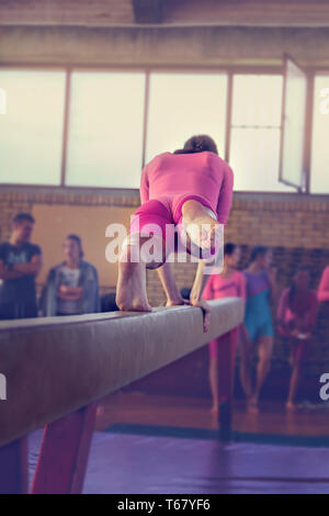 Young girl athlete gymnast on balance beam competition in gymnastics. Focus on feet - Image Stock Photo