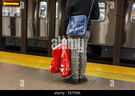 A shopper wearing his Marc Jacobs brand over-the-shoulder tote while carrying his  Century 21 off-price retailer purchases in the subway in New York on Saturday, April 20, 2019. (Â© Richard B. Levine) Stock Photo