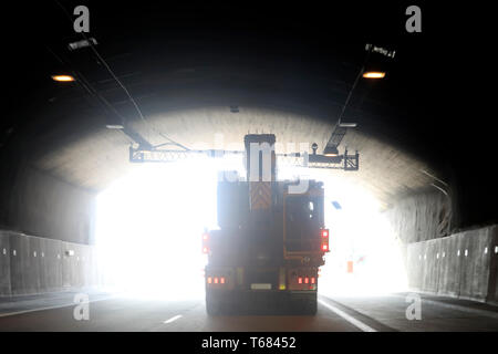 Semi trailer transporting an oversize load against light of day at the end of a freeway tunnel. Stock Photo