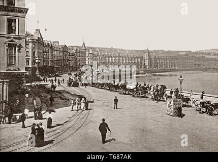 Late 19th Century views of  the busy Loch Promenade that runs nearly the entire length of beachfront in Douglas was constructed in 1878. Douglas is the capital, main commercial port and largest town of the Isle of Man,It grew rapidly as a result of links with the English port of Liverpool in the 18th century. It became a major tourist destination following the formation of the Isle of Man Steam Packet Company in 1830, which  led to greatly improved services, and also laid the foundations for growth in both cargo and tourist traffic. Stock Photo