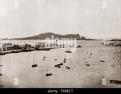 Late 19th Century view of Howth Harbour, a fishing village and outer suburb of Dublin, Ireland. Originally just a small fishing village, Howth with its surrounding once-rural district is now a busy suburb of Dublin, with a mix of suburban residential development, wild hillside and heathland, golf courses, cliff and coastal paths, a small quarry and a busy commercial fishing port. Stock Photo