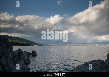 Rainbow in thunderstorm above Croatian coast, storm clouds over Rijeka and Opatija in dusk, calm seas and rocks in front, weather and climate concept Stock Photo