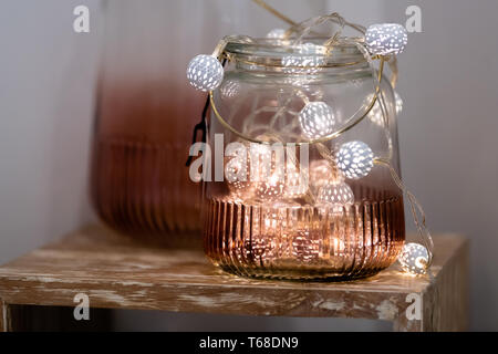 White and pink fairy tea lights in coloured glass jar with blurred background on display Stock Photo