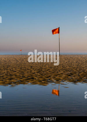 Red flag mirroring in water just after sunrise at a beach in northern France Stock Photo