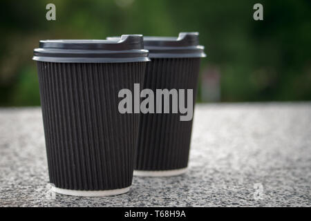 Two black disposable cups of coffee with lids are standing on the stone parapet, rest and a walk around the city, background or concept Stock Photo