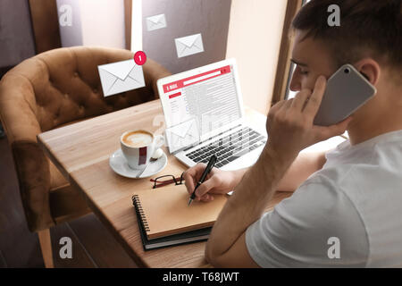 Young man talking on mobile phone while checking an email in cafe Stock Photo
