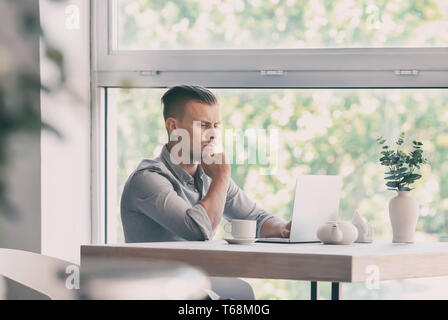 Troubled freelancer working on laptop in cafe Stock Photo