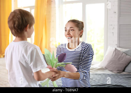 Mother receiving flowers from her cute little son at home Stock Photo