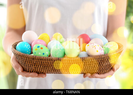 Young woman with wicker bowl full of colorful Easter eggs, closeup Stock Photo