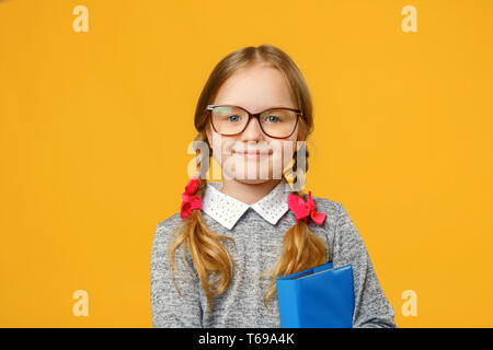 Closeup little girl schoolgirl on yellow background. The child is holding a book. The concept of education and school. Stock Photo