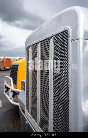 Big rig classic powerful American freight industrial semi trucks with chrome accessories and large grilles standing on the truck stop for rest and wai Stock Photo