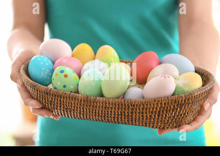 Young woman with wicker bowl full of colorful Easter eggs, closeup Stock Photo