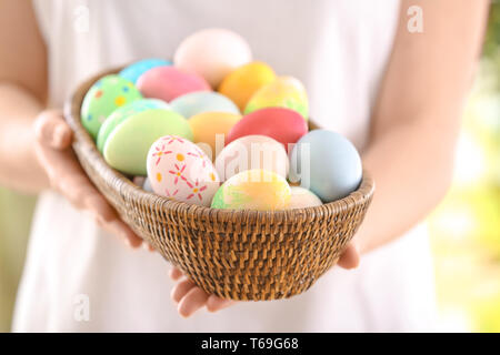 Young woman with wicker bowl full of colorful Easter eggs, closeup Stock Photo