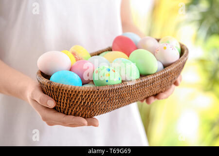 Young woman with wicker bowl full of colorful Easter eggs, closeup Stock Photo