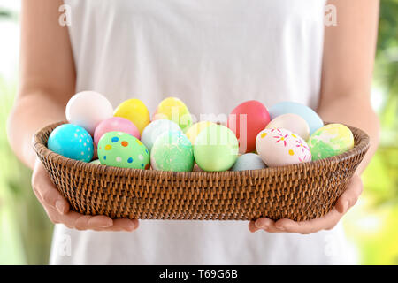 Young woman with wicker bowl full of colorful Easter eggs, closeup Stock Photo