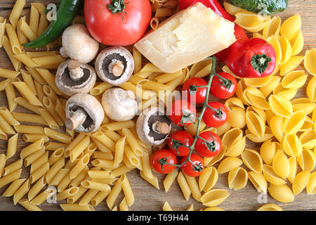 Different raw pasta with vegetables and cheese on table Stock Photo