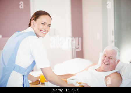 Portrait of nurse offering breakfast to senior man lying on bed Stock Photo