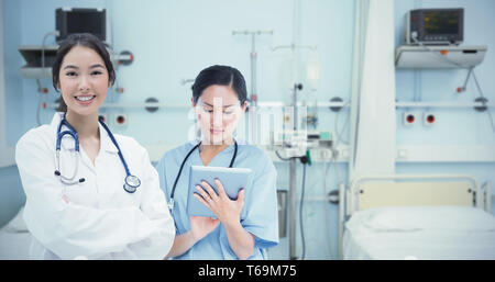 Composite image of surgeon using digital tablet with group around table in hospital Stock Photo