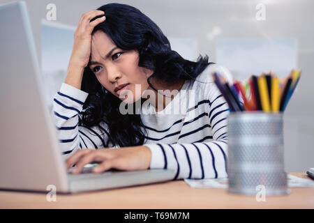 Composite image of concentrated asian woman with hand on head using laptop Stock Photo