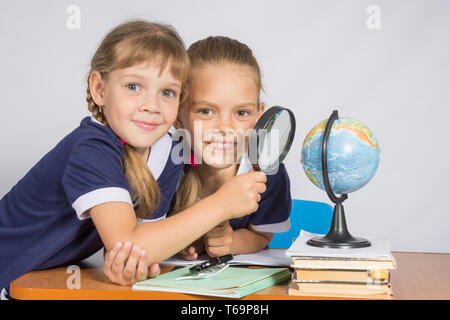 Two schoolgirls looking at globe through a magnifying glass Stock Photo
