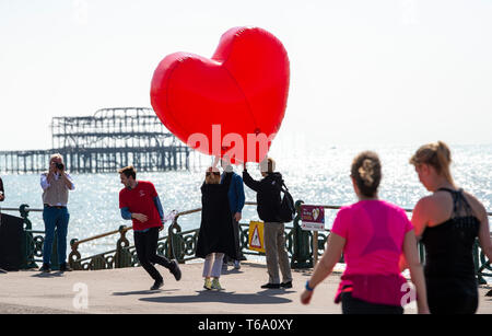 Brighton UK 30th April 2019 - An inflatable red heart is carried along Hove seafront to promote the 'Run for Love ' event which takes place on 1st June as they enjoy the warm sunny weather this morning with it forecast to reach into the high teens in some parts of the South East today. Credit: Simon Dack/Alamy Live News Stock Photo