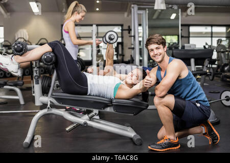 Trainer man helping woman doing her crunches and showing thumbs up Stock Photo