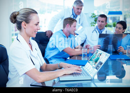 Composite image of beautiful smiling doctor typing on keyboard with her team behind Stock Photo