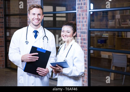 Portrait of doctors standing near library with clipboard and digital tablet Stock Photo