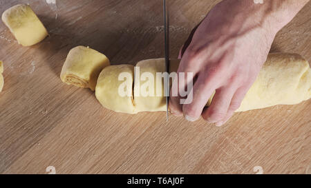 Pastry chef cuts roll with cinnamon, sugar and butter on portions to bake cinnamon rolls. Hands close-up. Stock Photo