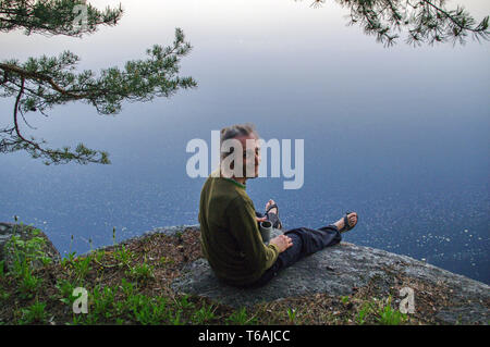 happy young man sitting on a rocky slope above lake Stock Photo