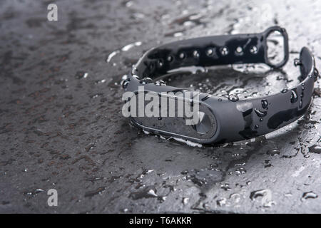 wet fitness bracelet, fitness tracker on a black slate background with drops of water Stock Photo