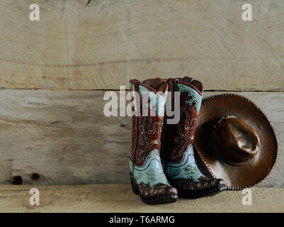 teal and brown cowboy boots and hat laying on a bed of leaves Stock Photo