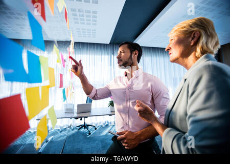Side view of two business people looking at post it wall Stock Photo