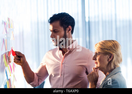 Side view of two business people looking at post it wall Stock Photo