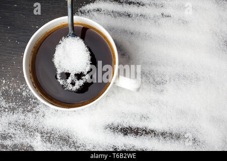 unhealthy white sugar concept. Scull spoon with sugar and cup of black coffee on wooden background Stock Photo