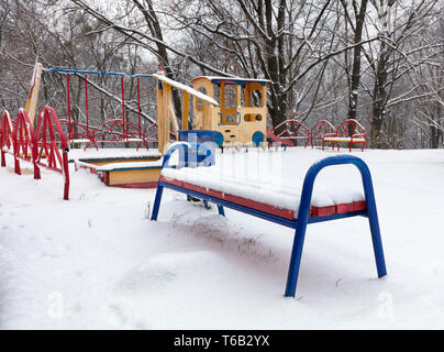 Snow covered the bench and multicolored children's playground in the courtyard of the winter park Stock Photo